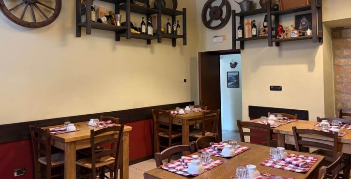 Sala ristorante rustica con tavoli in legno, tovagliette a quadri e decorazioni vintage.