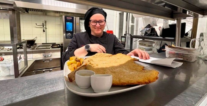 Chef presenta una grande cotoletta di vitello impanata con patate arrosto in cucina professionale.