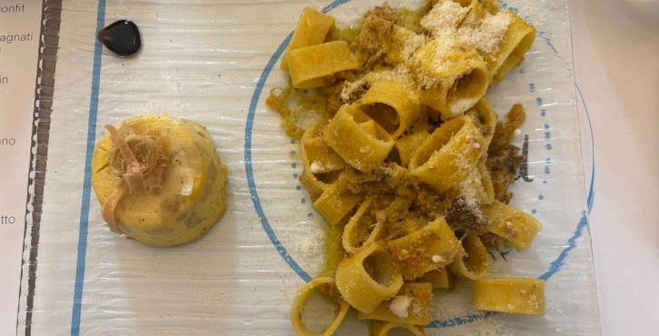 Pasta fresca a nastro con ragù di carne e formaggio grattugiato servita su piatto decorativo.