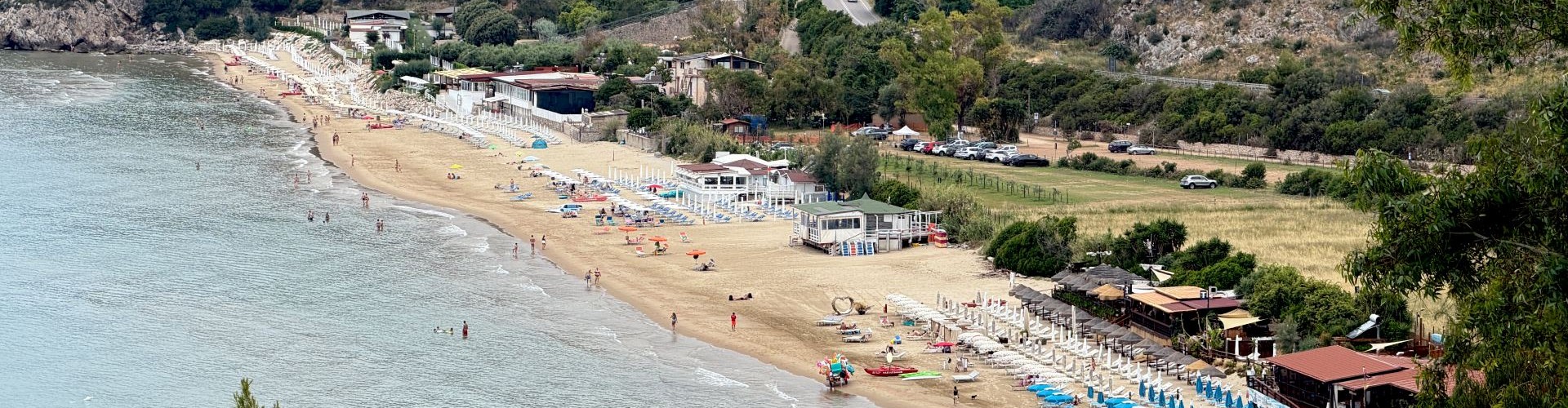 Vista panoramica di spiaggia sabbiosa, mare tranquillo e colline costiere.