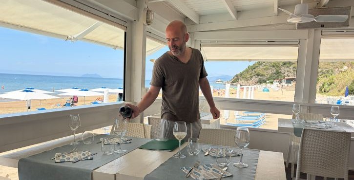 Sala del ristorante con vista sulla spiaggia mentre un addetto prepara i tavoli.