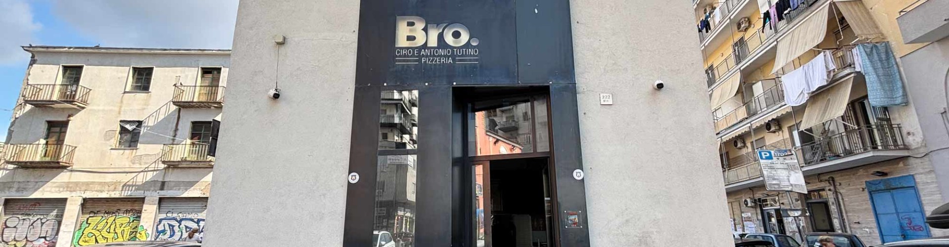 Facciata della pizzeria Bro con ingresso moderno e auto parcheggiate in zona residenziale.