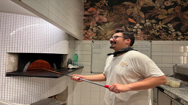 Chef sorridente mentre inforna la pizza in un forno a legna rivestito di piastrelle.