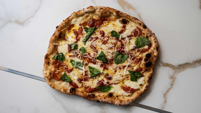 Pizza napoletana con formaggio fuso, pomodorini e foglie di basilico fresco su marmo.