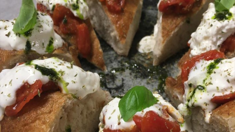 Bruschetta tostata con burrata, pomodori e basilico servita su piatto da portata.