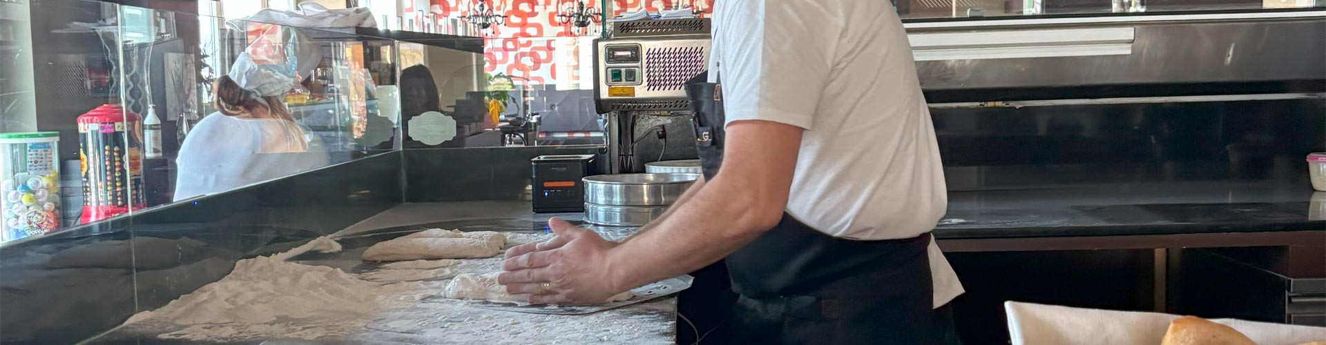Chef modella l’impasto della pizza su un piano infarinato in una cucina a vista.