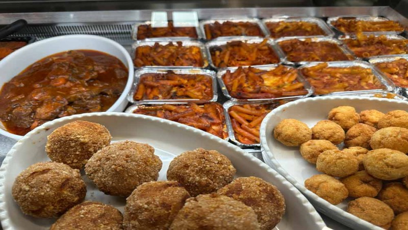 Selezione di piatti italiani da asporto con arancini, pasta al forno e carne brasata da Deliziamoci.