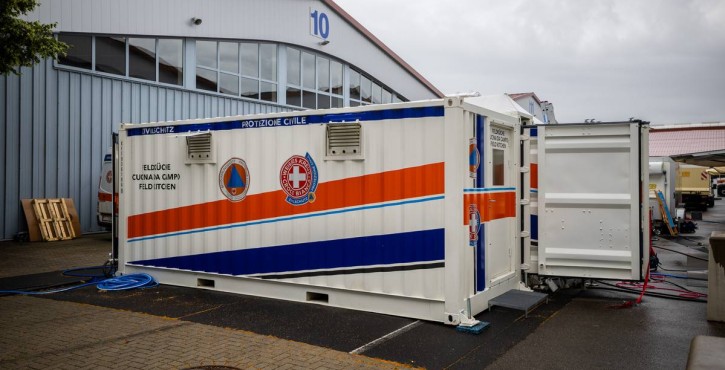 Mobile field kitchen container of the White Cross with civil protection markings outside an industrial hall.