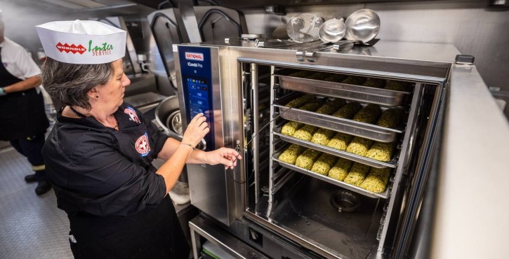 Chef operating RATIONAL iCombi Pro combi oven filled with trays of herb dumplings.