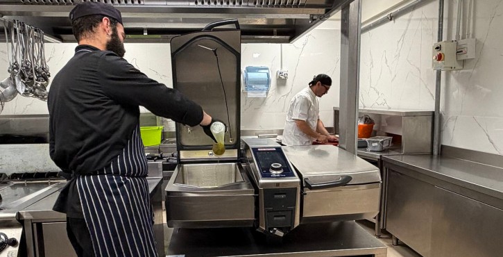 Chef versa ingredienti in un RATIONAL iVario mentre una collega prepara il cibo nella cucina professionale.