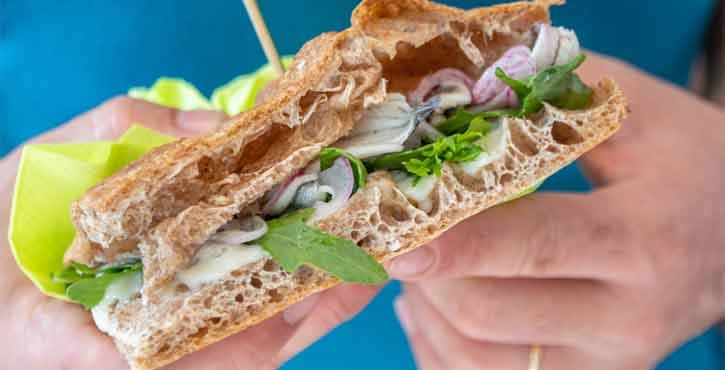 Primo piano di un panino con pesce fresco, erbe aromatiche e cipolle in pane artigianale.
