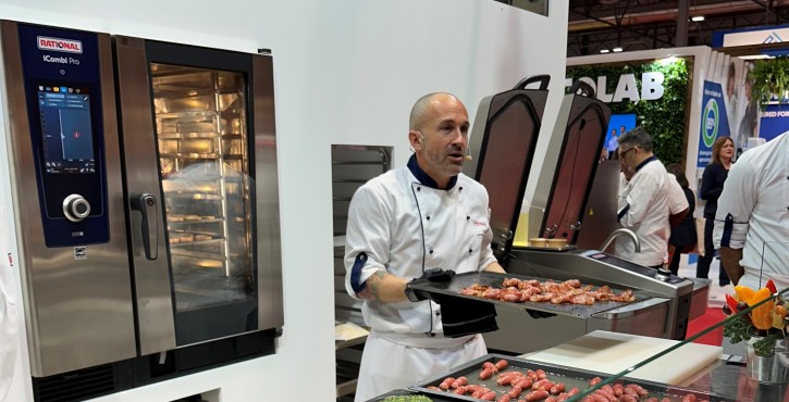 Chef presentando salchichas cocinadas junto al RATIONAL iCombi Pro vaporizador combinado y RATIONAL iVario Pro.