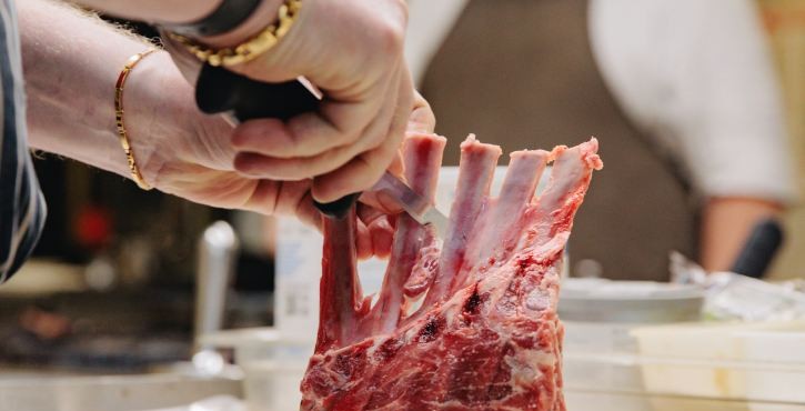 Chef rifila un carré di agnello in cucina professionale prima della cottura.