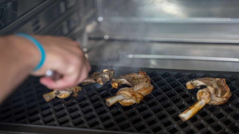 Chef griglia costolette di agnello sulla piastra di un RATIONAL iCombi Pro forno professionale.