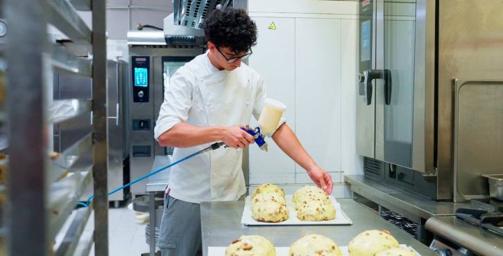 Pasticcere spruzza glassa sull'impasto vicino al RATIONAL iCombi Pro forno professionale.