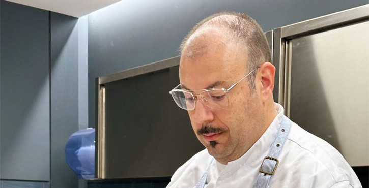 Chef con occhiali concentrato nella preparazione dei piatti in cucina professionale.