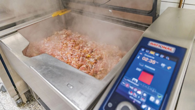 RATIONAL iVario podczas gotowania mięsa, z unoszącą się parą w profesjonalnej kuchni.