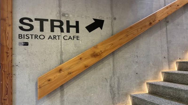 Schody betonowe z drewnianą poręczą i napisem prowadzącym do STRH Bistro Art Café na piętrze.