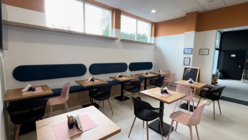 Jasne nowoczesne bistro z nakrytymi stołami, czarnymi i różowymi krzesłami oraz dużymi oknami.