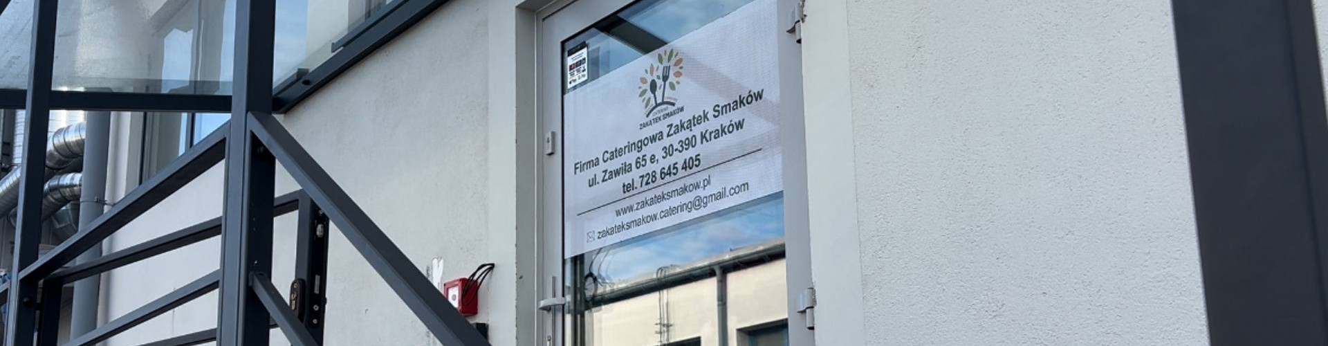 Wejście do firmy cateringowej Zakątek Smaków z logo i danymi kontaktowymi na szklanych drzwiach.