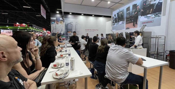 Visitantes acompanham uma aula-show com RATIONAL iCombi Pro forno combinado em estande movimentado da feira.