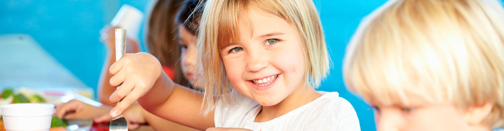 Smiling child eating a healthy meal with other children at a bright table.