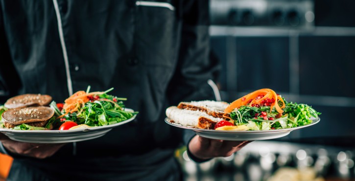 Chef en uniforme noir tenant des assiettes de plats véganes bio avec salades fraîches.