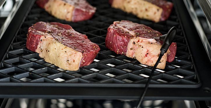 Steaks cooking on a grill with a core temperature probe inserted.