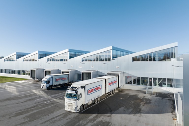 RATIONAL logistics trucks being loaded at a modern warehouse under blue sky.