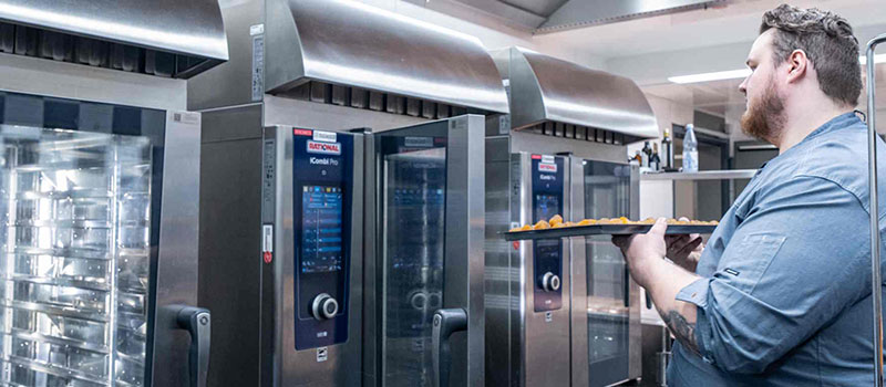 Koch schiebt Blech in RATIONAL iCombi Pro Kombidämpfer in Profiküche.
