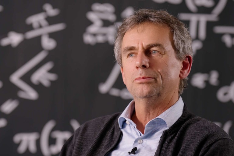 Professor vor Tafel mit mathematischen Formeln im Interview.