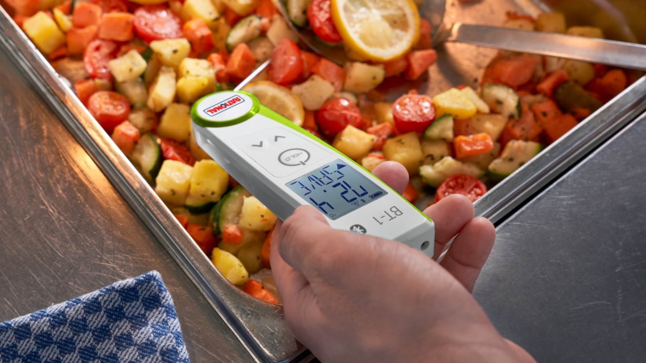 Hand holding RATIONAL food thermometer over tray of roasted vegetables.