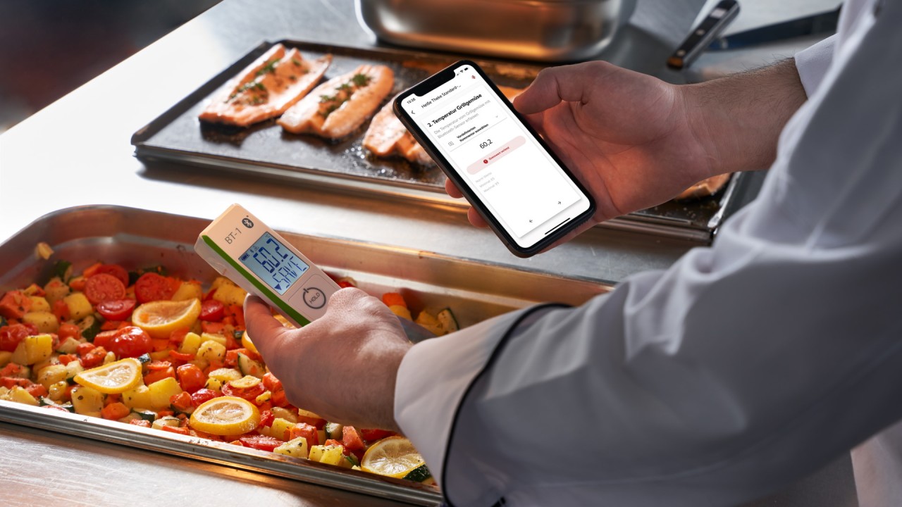 Chef checking food temperature with RATIONAL thermometer and smartphone app.
