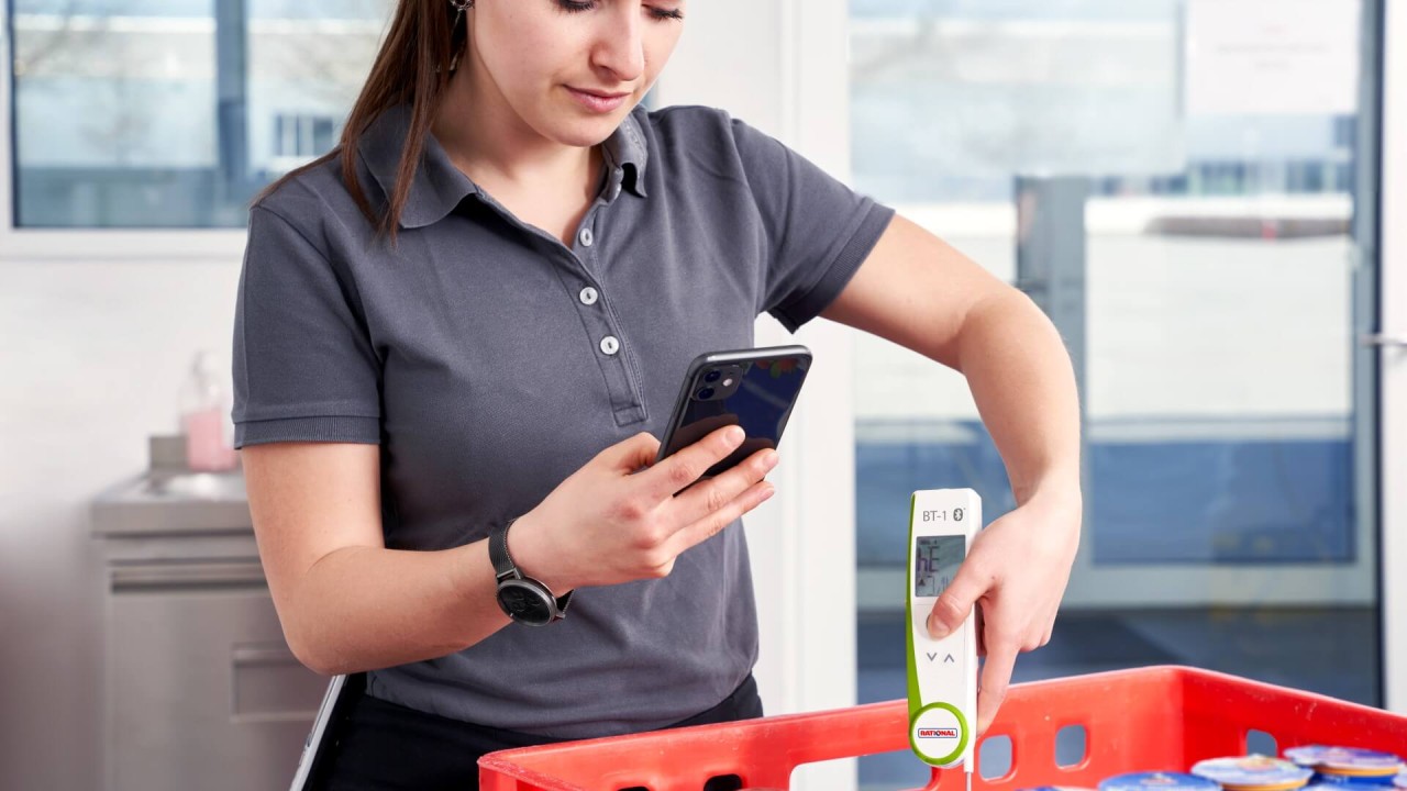 Woman checking chilled products with RATIONAL thermometer and smartphone.