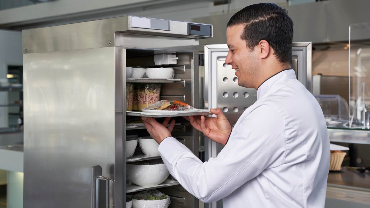 Chef placing a prepared meal tray into a stainless steel holding cabinet.