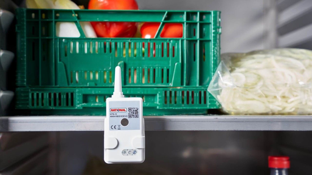 RATIONAL sensor clipped to a refrigerator shelf beside fresh vegetables and sliced onions.