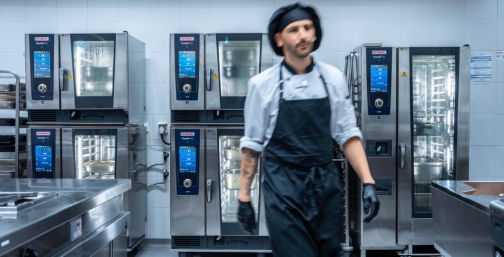 Un chef marche dans une cuisine avec plusieurs fours RATIONAL iCombi Pro en arrière-plan.
