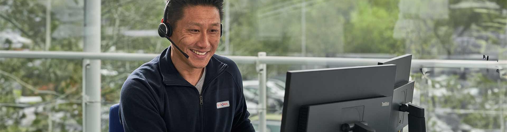 Ein Kundenservice-Mitarbeiter lächelt, während er am Telefon spricht, mit einem Computerbildschirm vor sich in einem Büro.