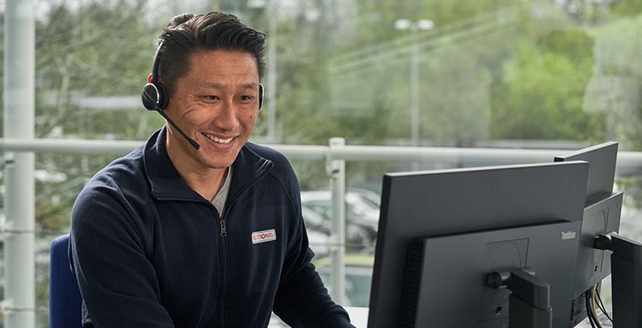 Ein Kundenservice-Mitarbeiter lächelt, während er am Telefon spricht, mit einem Computerbildschirm vor sich in einem Büro.