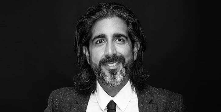 Portrait of Ashwin Kamlani, smiling in formal attire against a dark background.