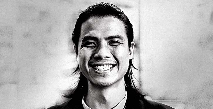 Portrait of Brandon Kua, smiling broadly with long hair and wearing a dark shirt.