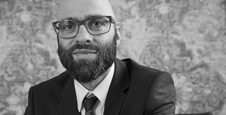 Portrait of Daniel Gantenberg, in a suit with glasses and beard.