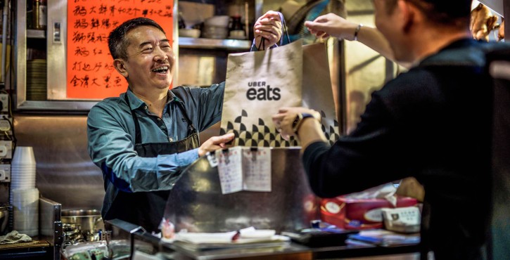 A smiling employee hands over an Uber Eats bag to a person in an Asian restaurant
