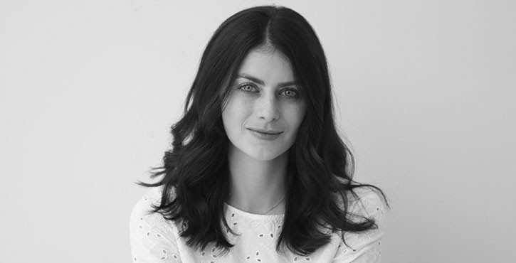 Black-and-white image of a woman with dark hair and a white top, smiling softly at the camera.