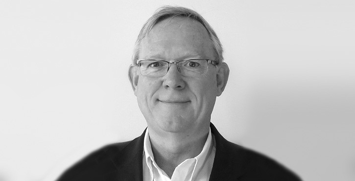 Portrait of a middle-aged man with glasses and short grey hair, smiling and wearing a dark suit.