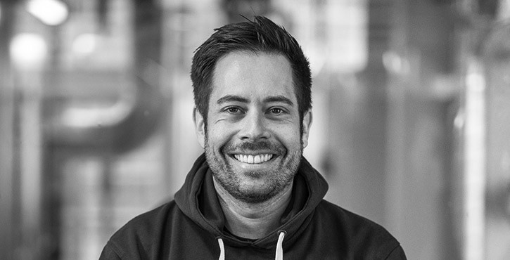 Black and white portrait photo of a smiling man with short hair and a hoodie.