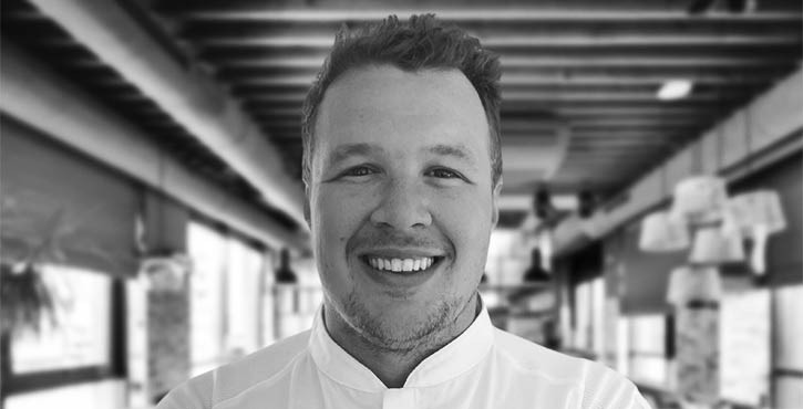 Black and white portrait of Chef Penfold smiling in a restaurant setting.