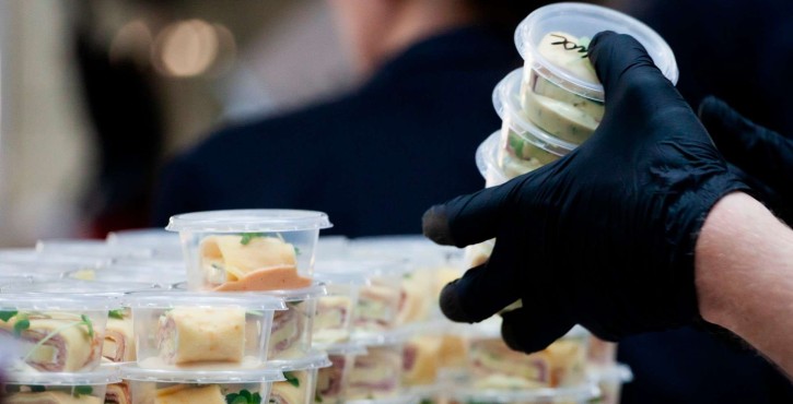 Gloved hand stacks several small plastic containers filled with wraps.