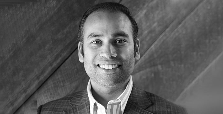 A man in a checkered suit smiling directly at the camera.