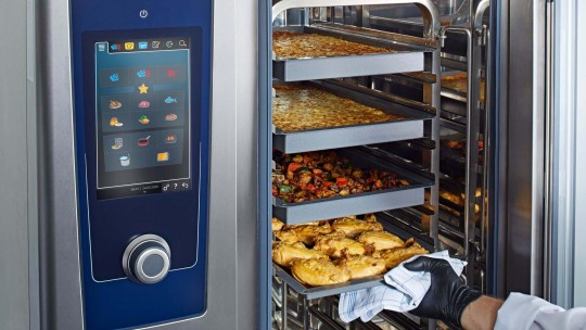 Open Rational iCombi Pro combi-steamer with trays full of baked dishes.